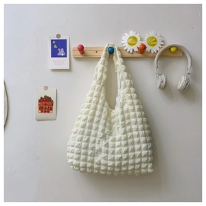 Detail of white pleated cloud bag with square texture hanging on a wooden hook