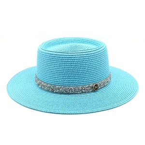 Close-up of sky blue straw boater hat featuring a shimmering rhinestone band and M metal logo