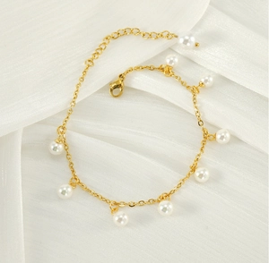 Detailed shot of 18K gold tassels and white pearls anklet on white folded silk fabric