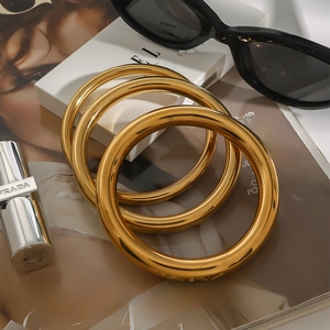 Three chunky 18k gold plated stainless steel round bangles in a minimalist luxury style
