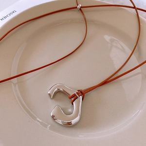 Close-up of irregular silver C-shaped pendant with brown leather cord on ceramic tray