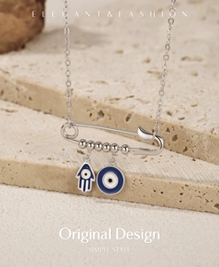 Detail of silver safety pin necklace with blue Hamsa hand and Evil Eye charms on stones