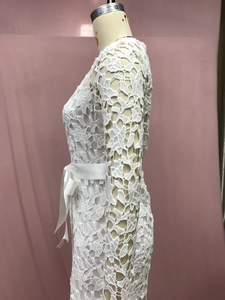 Detail of white hollow lace dress featuring a satin waist tie and intricate floral texture