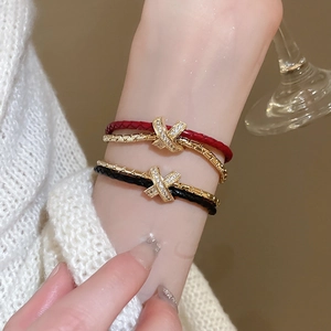 Gros plan de bracelets croisés dorés avec lanières en cuir rouge et noir et zircons brillants