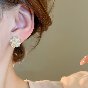 Close-up of elegant gold flower stud earrings with pearls and zircon on model's ear