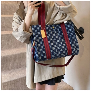 Close-up of blue checkered tote bag featuring red canvas straps and gold flower button