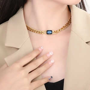 Detail van gouden Cubaanse choker ketting met rechthoekig blauw kristal op het sleutelbeen