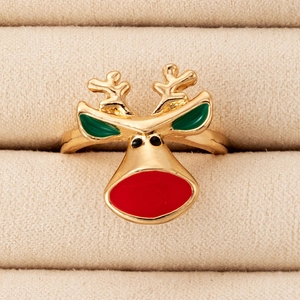 Close-up of golden reindeer ring with red and green enamel details on soft beige velvet