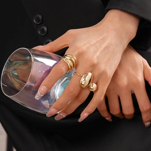 Detail of layered gold rings and a teardrop design on model holding a glass