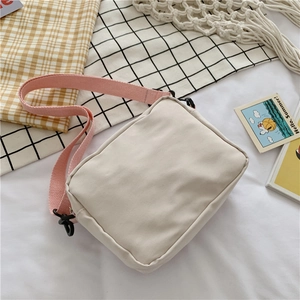 Detail view of a beige canvas crossbody bag with an adjustable pink woven strap and hooks