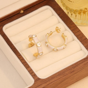 Detailed close-up of golden C-shaped earrings with white enamel and sparkling zircons
