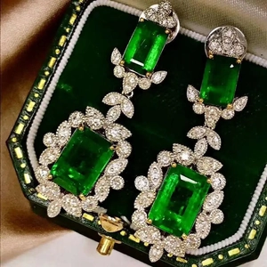 Detail of luxury emerald green zircon earrings in a vintage jewelry box with silk fabric