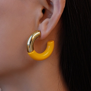 Close-up of gold-toned acrylic C-shaped earrings worn by a model for a stylish look