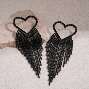 Macro shot of black rhinestone heart earrings with long tassels on a textured stone