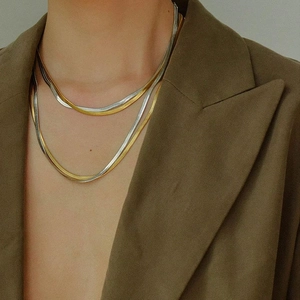 Close-up of double-layered gold and silver flat snake bone chain necklaces on a model