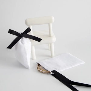 Detail of white linen jewelry pouch with black ribbon and gold bracelet