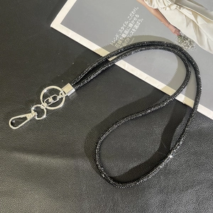Detail of black glitter crossbody phone strap with silver lobster clasp on a textured surface
