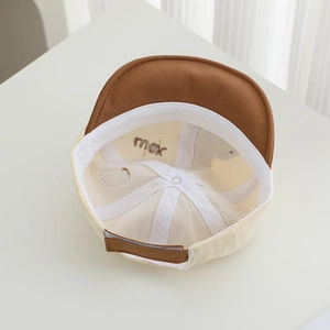 Detail of baby baseball cap interior showing seams and rock embroidery on beige fabric