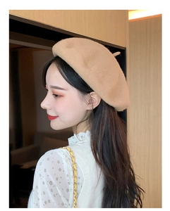 Side view of a woman wearing a beige wool beret hat in a cozy indoor setting
