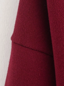 Detaillierte Makroansicht der Schulternähte und Textur des dunkelroten Strick-Cardigans