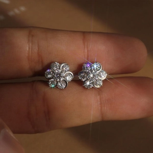 Macro shot of sparkling flower stud earrings with brilliant zircon stones held by fingers