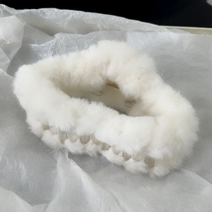 Close-up of white plush hair claw clip with soft faux fur and acrylic frame on textured paper