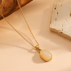 Dettaglio della collana dorata con pendente ovale in opale bianco su base in pietra