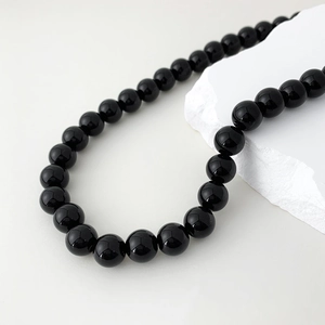 Detail view of smooth black agate beads necklace resting on white textured stone surface