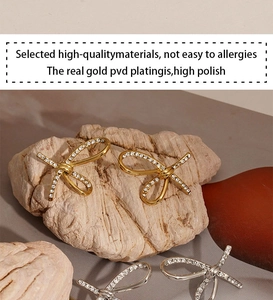 Detailed close-up of crystal bow earrings with PVD gold plating on a textured stone base