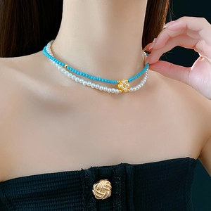 Dettaglio collana a due strati con perle bianche, perline blu e ciondolo a fiore dorato