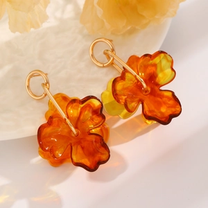 Detailed close-up of amber flower earrings with gold hoops on a ceramic plate