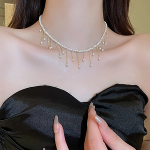 Detail of a multi-strand pearl choker with gold tassel pendant on a woman's collarbone
