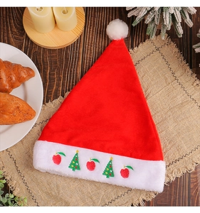 Detail of red plush Christmas hat with apple and tree embroidery on a festive wooden table