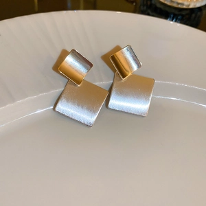 Close-up of geometric gold and brushed silver studs on a white textured plate