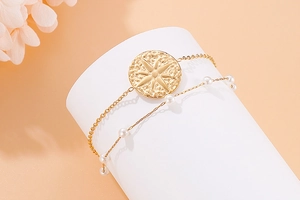 Detail of a double-layer gold bracelet featuring a sunburst pendant and white pearls