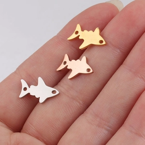 Three small shark pendants in gold, rose gold, and silver stainless steel on a finger