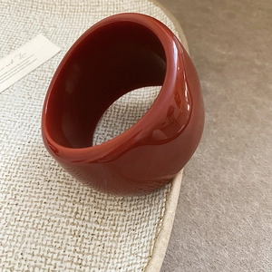 Macro shot of thick dark red resin bangle with glossy finish on woven background