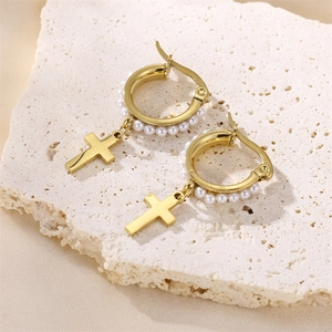 Detailaufnahme goldener Creolen mit Perlen und einem minimalistischen Kreuzanhänger