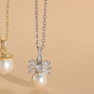 Detailed close-up of pearl pendant with zircon bow knot in gold and silver finish