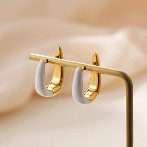 Close-up of gold U-shaped earrings with white enamel detail on a metal display stand