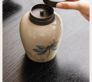 Close-up of hand opening a ceramic tea canister with hand-painted lotus flower patterns