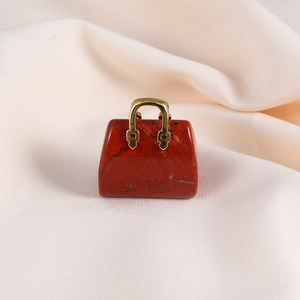 Detail view of mini red gemstone handbag charm with gold handle on beige fabric