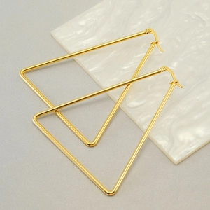 Polished gold stainless steel triangle hoop earrings on white marble background