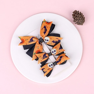 Detail of Halloween bow hair clips featuring pumpkin and bat motifs on a white card