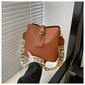 Detail of brown litchi pattern bucket bag featuring a wide patterned strap and gold hardware