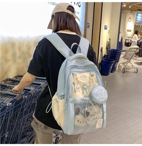 Detail view of a blue and white school backpack with clear pocket and plush charms