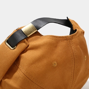 Detail of khaki canvas cap with black leather back strap and brass metal buckle closure