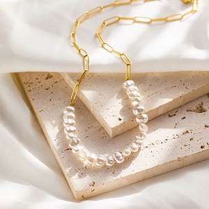 Detailed shot of an irregular pearl and gold paperclip chain necklace on white silk cloth