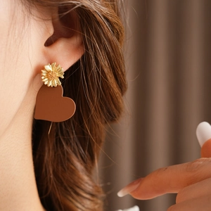 Close-up of a model wearing a gold daisy flower and brown heart drop earring