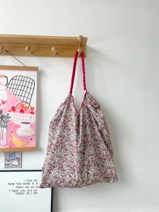 Floral canvas tote bag hanging on a wooden hook featuring a pink drawstring closure
